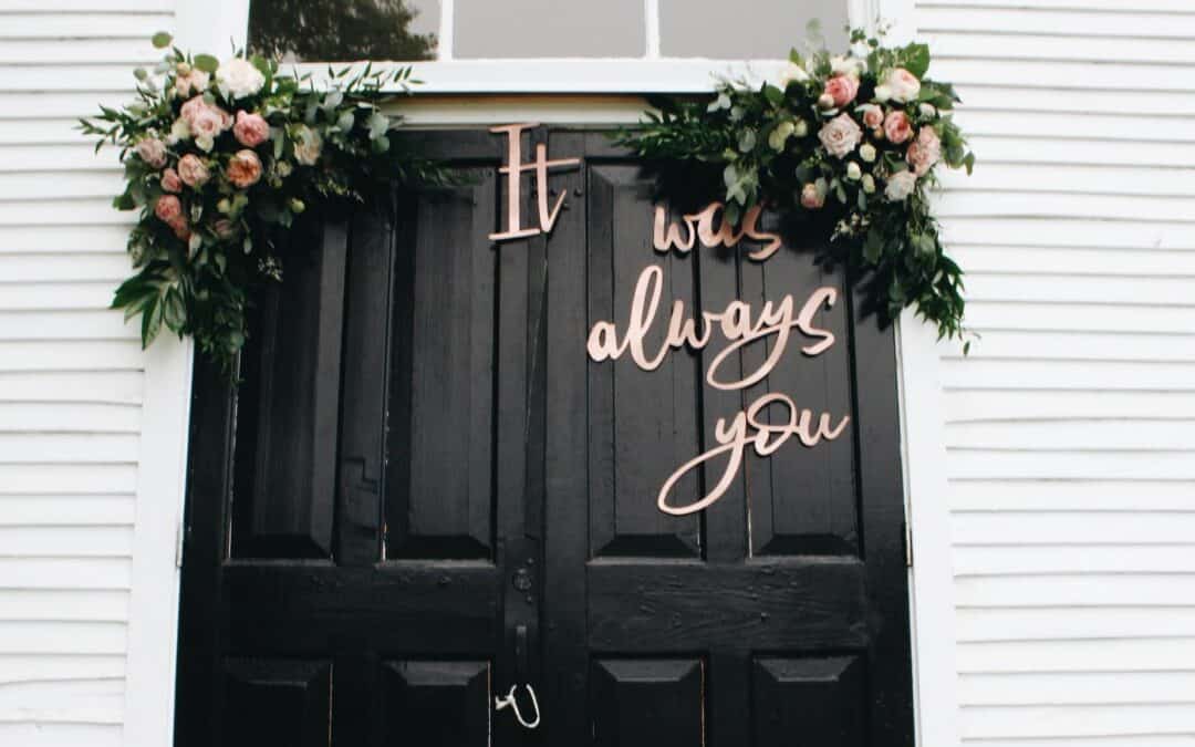 Black doors with floral arrangements and the words "It was always you" in cursive letters.