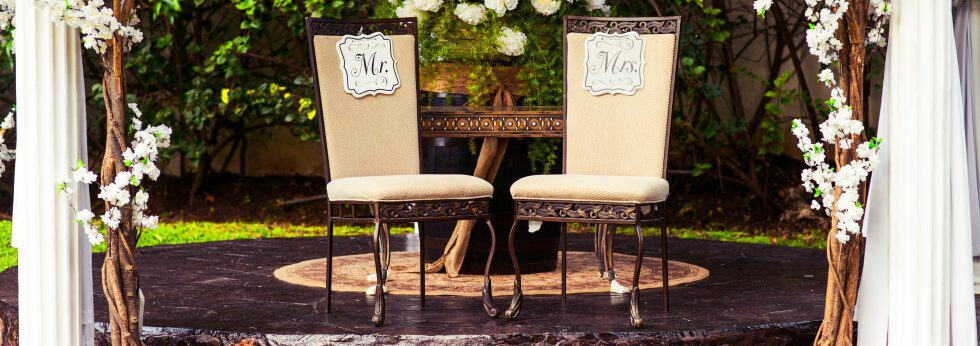 Two chairs with "Mr." and "Mrs." signs on a small platform, surrounded by floral decorations.